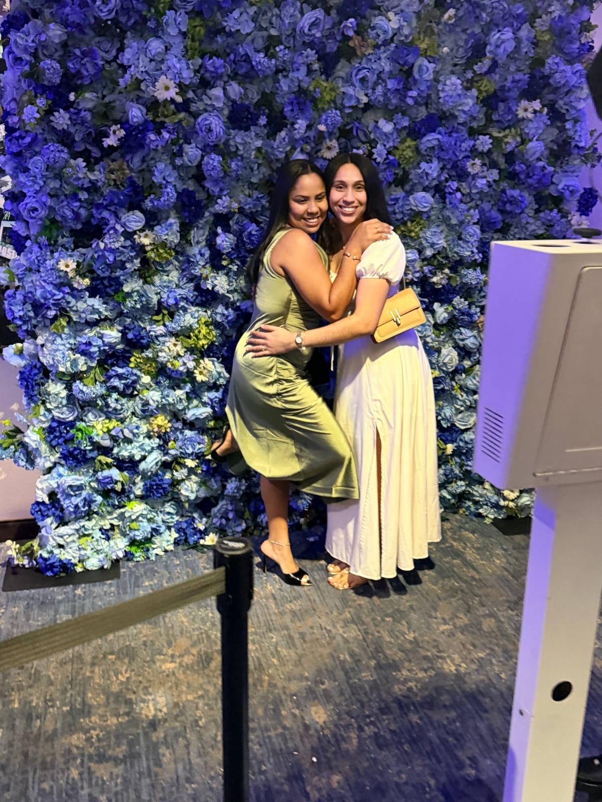 Two guests hugging in front of the blue flower wall at a New York event
