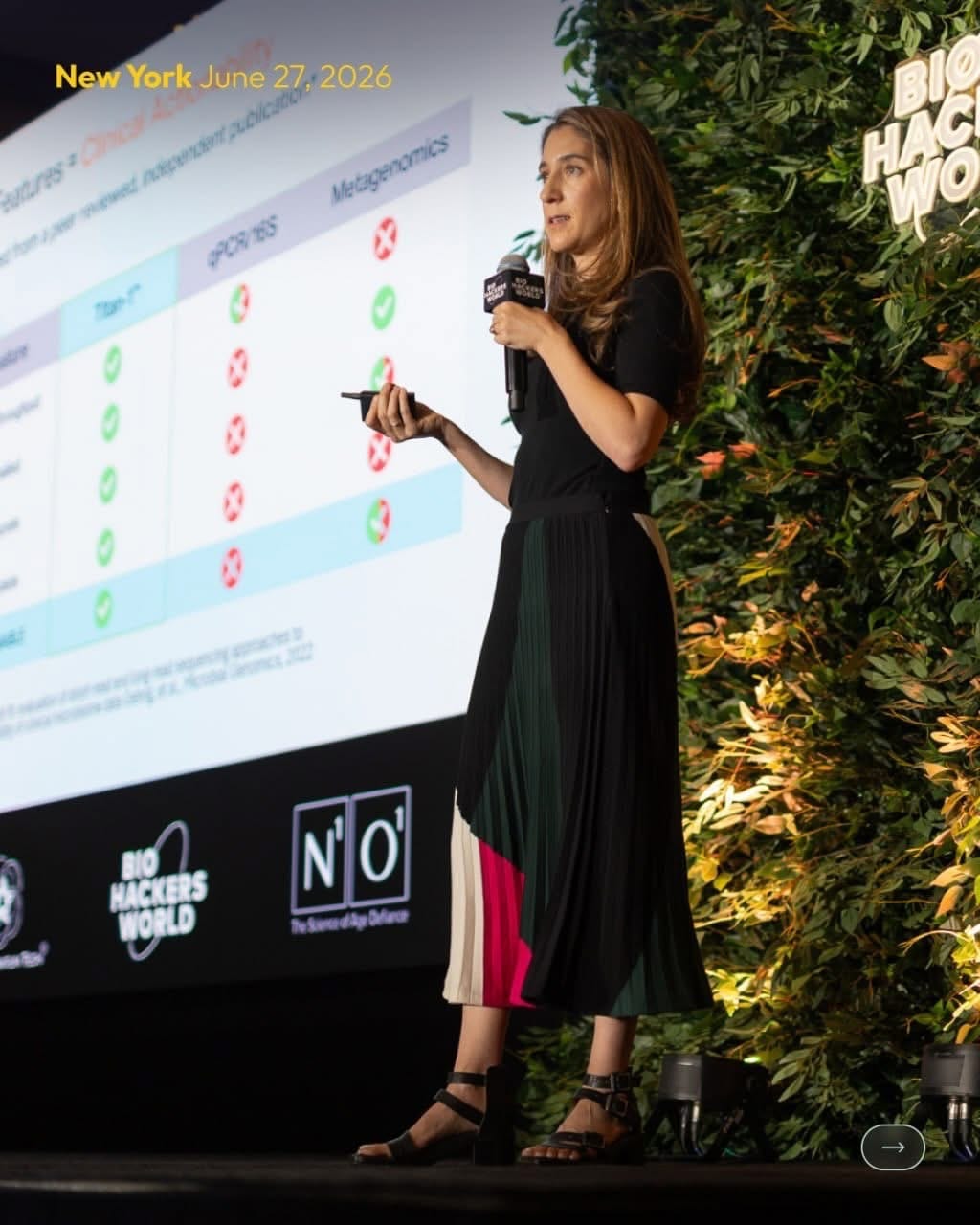 Presenter on stage beside the greenery hedge wall backdrop