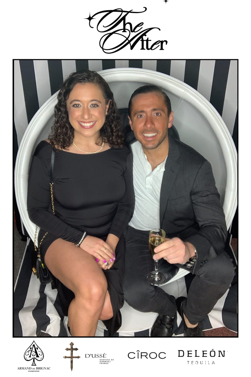 Couple posing at THE AFTER — black and white striped step-and-repeat, holding a champagne glass