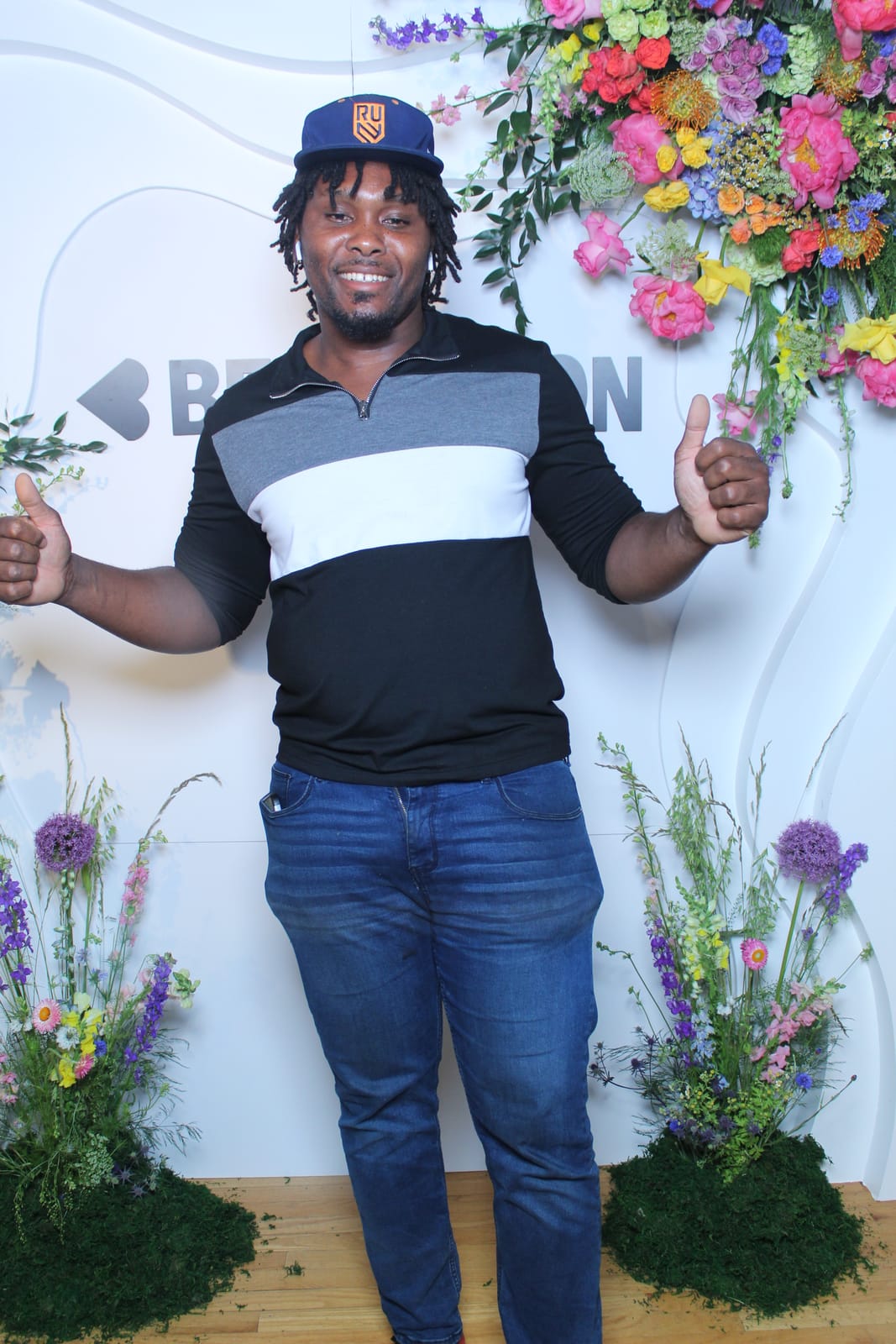 Guest giving thumbs up at the Beautycon photo booth — floral logo step-and-repeat
