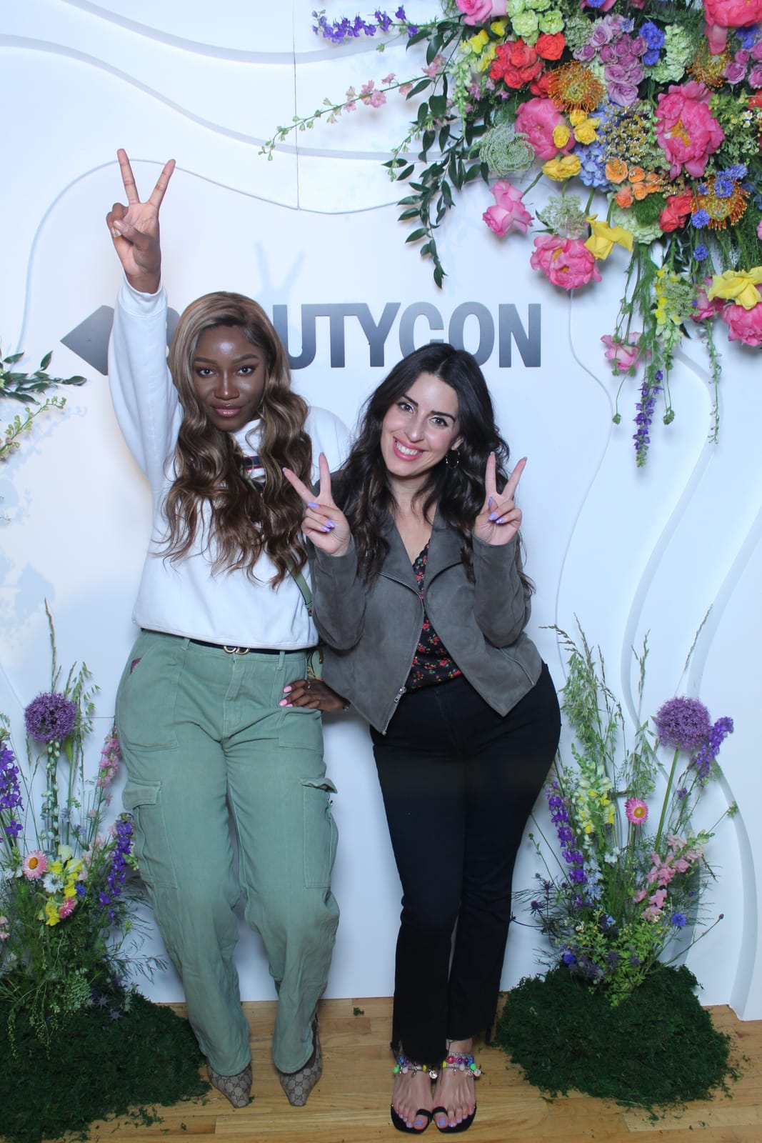 Two attendees flashing peace signs at the Beautycon floral wall