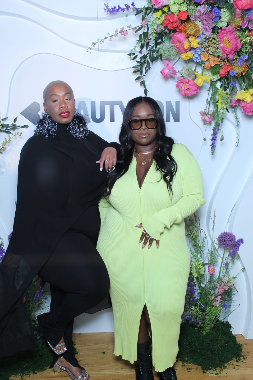 Two guests posing at the Beautycon floral logo wall