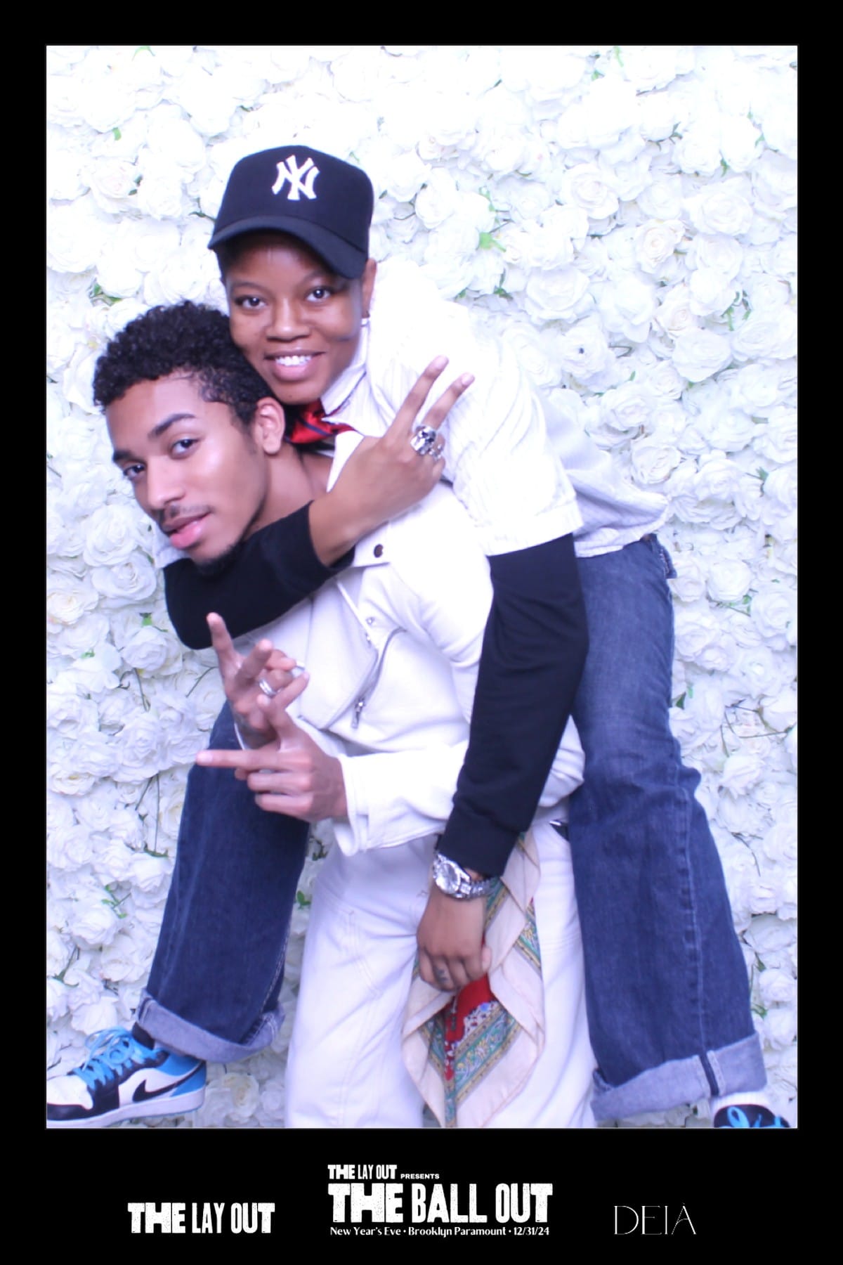 Piggyback pose at The Ball Out photo booth — white rose wall