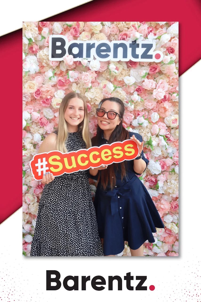 Two guests holding a Success prop at the Barentz flower wall