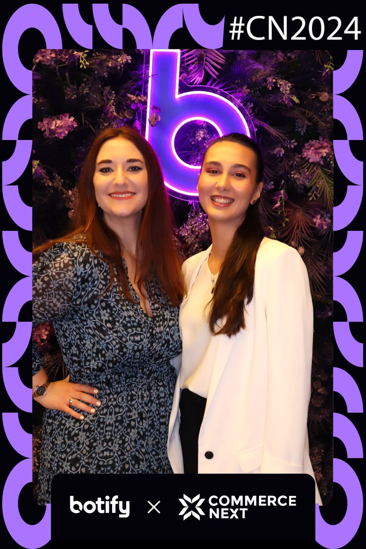 Two attendees smiling at the Botify x CommerceNext purple neon flower wall