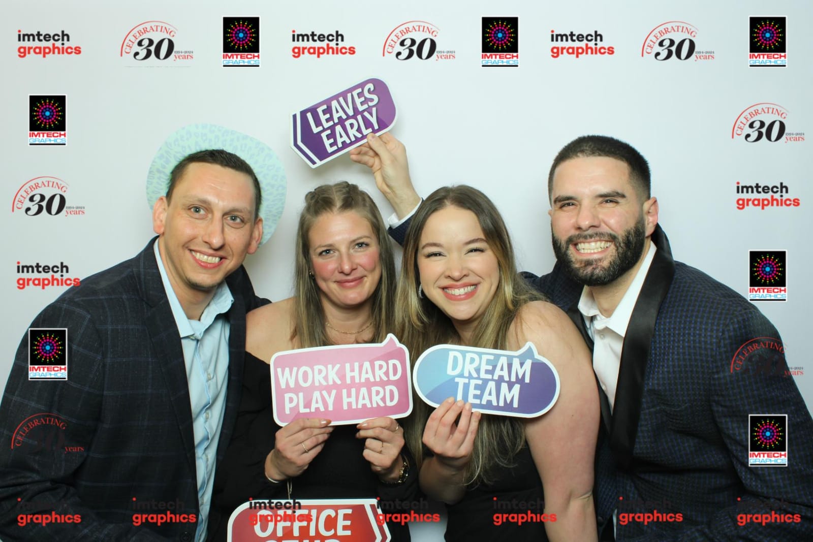 Group holding Work Hard Play Hard and Dream Team props at the Imtech Graphics 30th anniversary booth