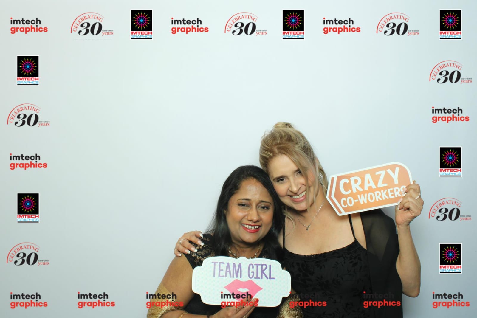 Two colleagues posing with a Team Girl prop at the Imtech Graphics photo booth