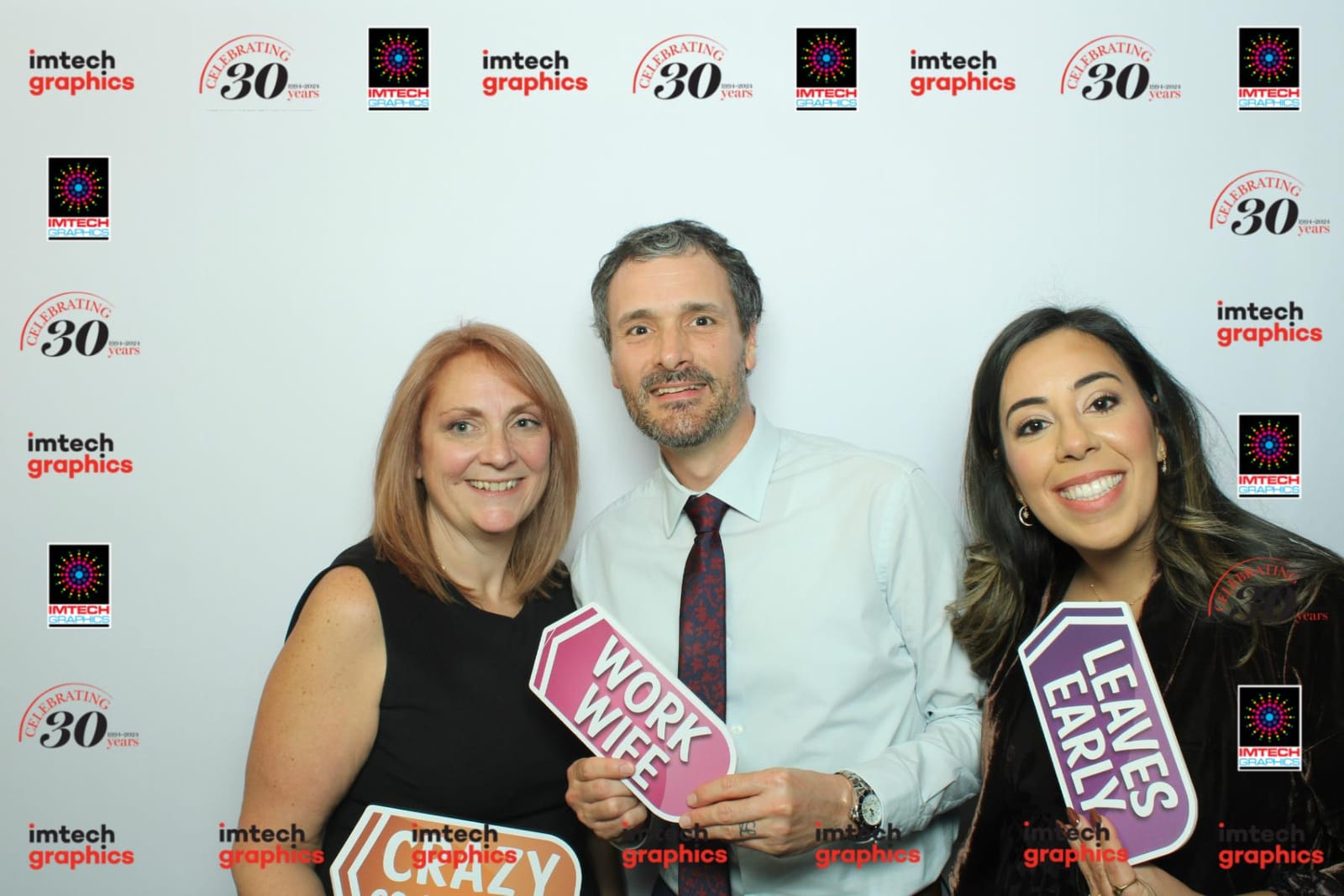 Colleagues posing with a Work Wife prop at the Imtech Graphics step-and-repeat