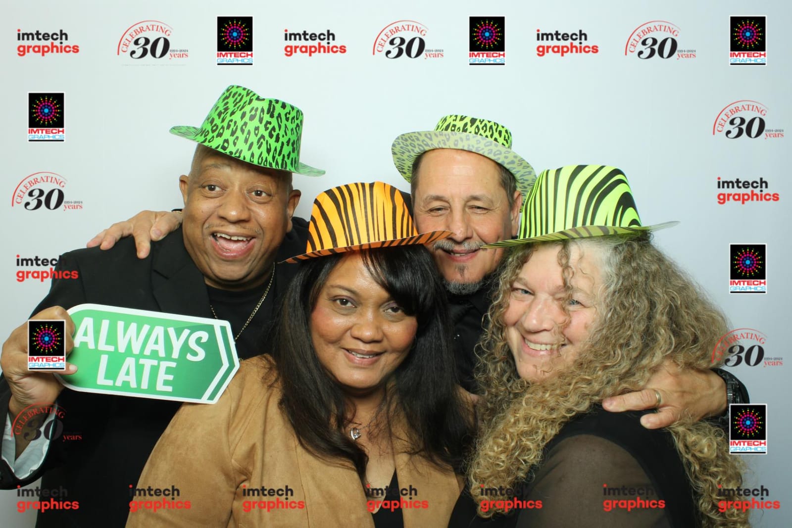 Four colleagues in animal-print hats holding an Always Late prop at the Imtech Graphics anniversary booth