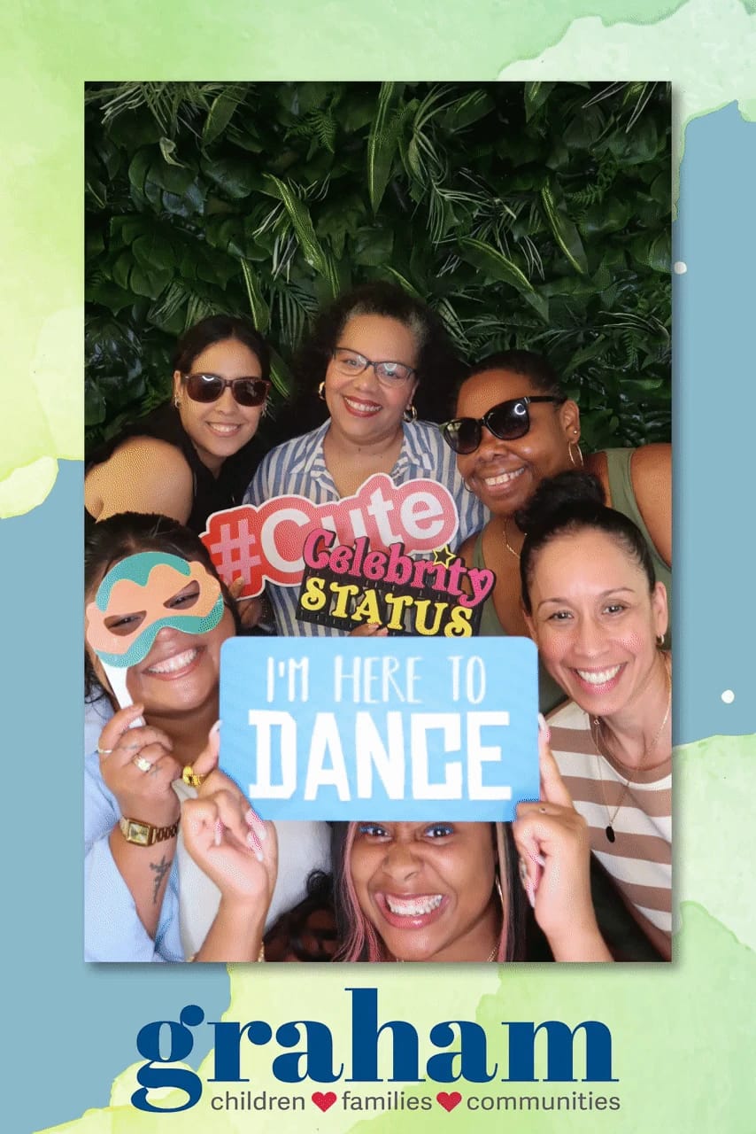 Six colleagues with props at the Graham staff celebration — greenery wall photo booth