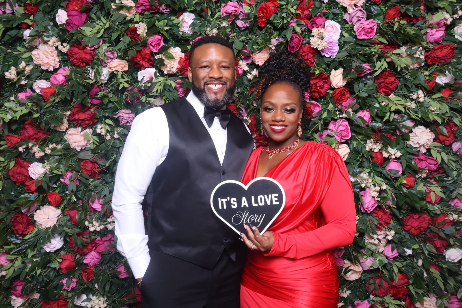Couple posing with an It's a Love Story heart sign at the wedding reception photo booth