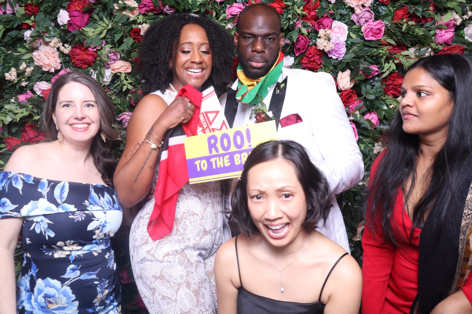 Group posing with a Roo to the Bride sign at the Love Story rose flower wall