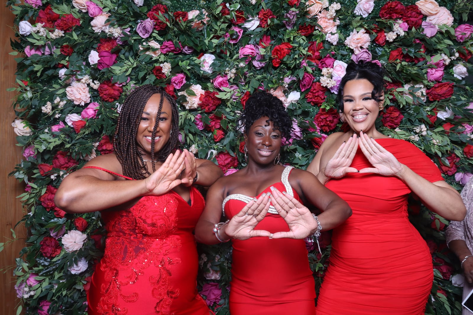 Three guests in red dresses posing at the Love Story rose flower wall
