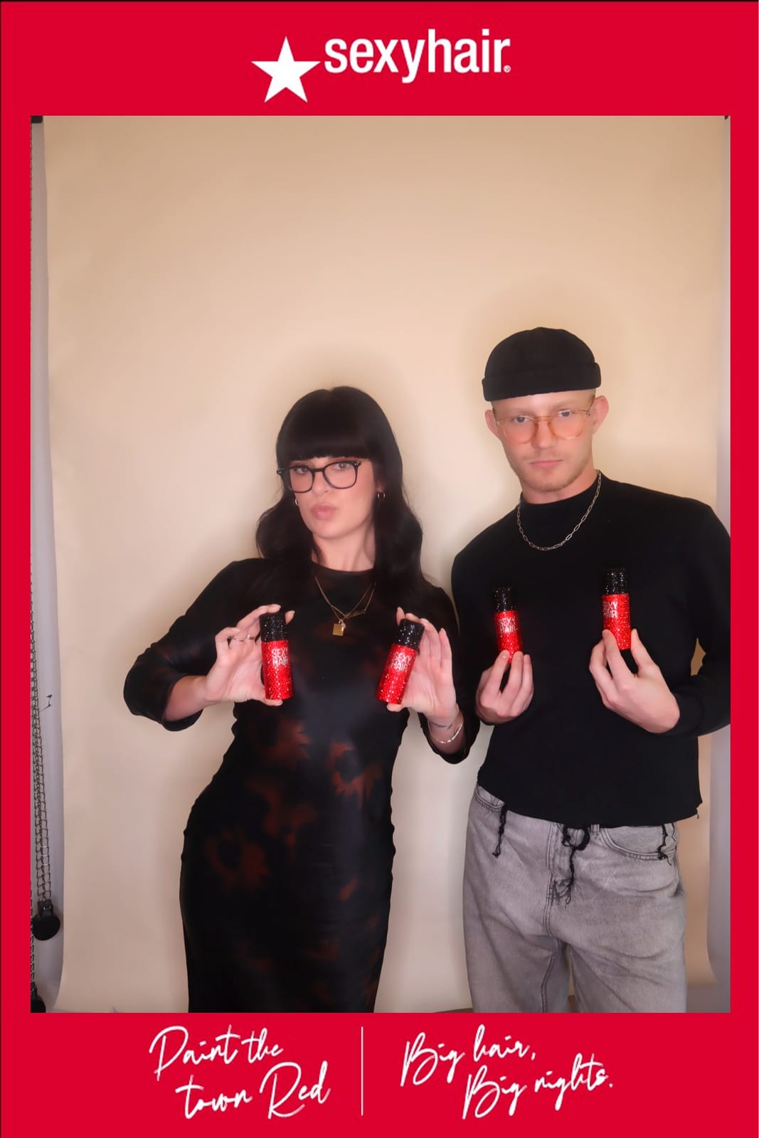 Two guests holding SexyHair styling products at the Paint the Town Red photo booth
