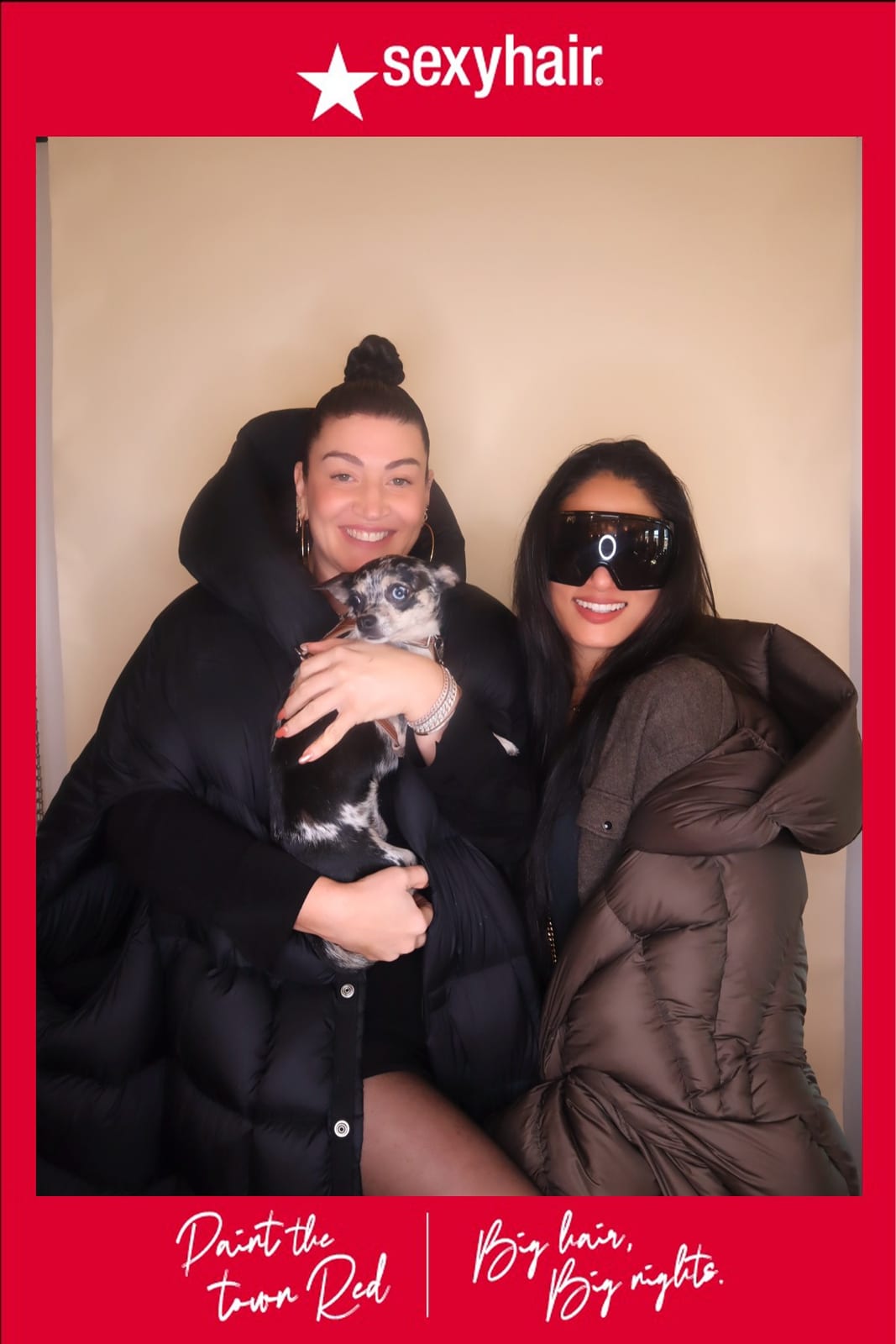 Two guests posing with a small dog at the SexyHair Paint the Town Red booth