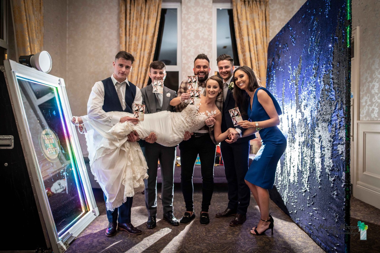 Wedding party celebrating in front of the mirror photo booth with a sequin backdrop