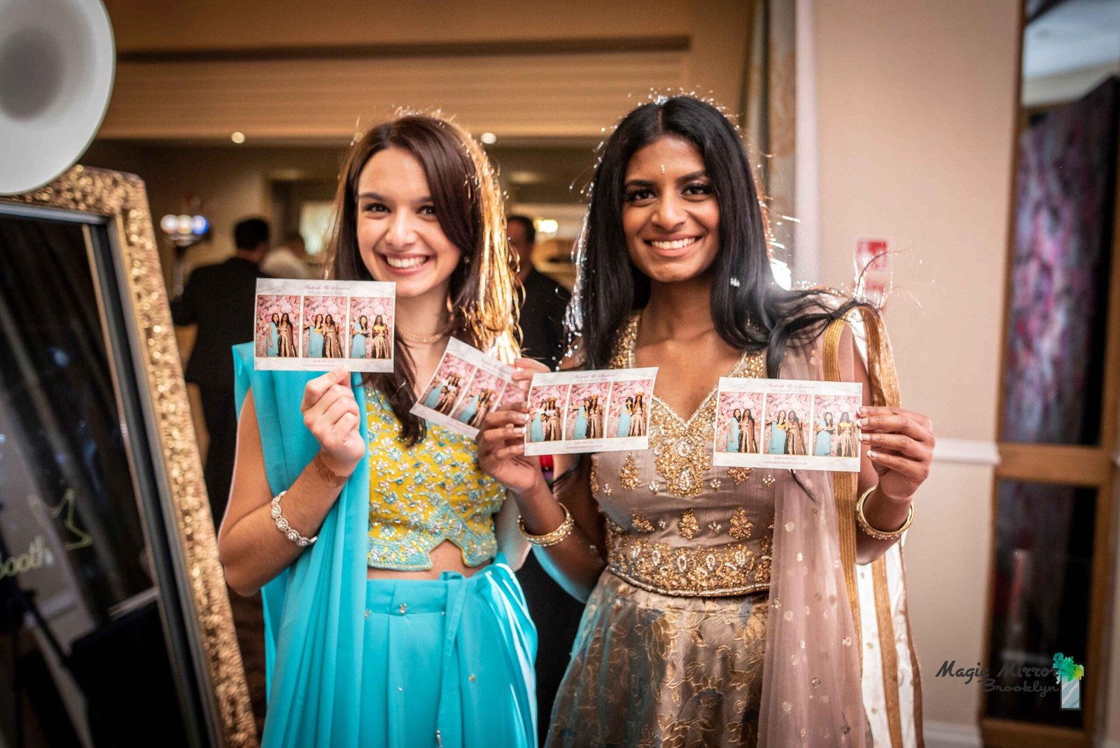 Two guests holding their photo strips beside the gold mirror booth