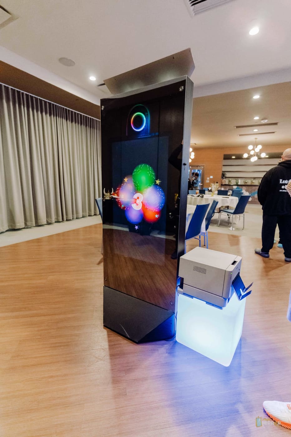 Mirror X booth mid-countdown with its instant printer on an LED plinth